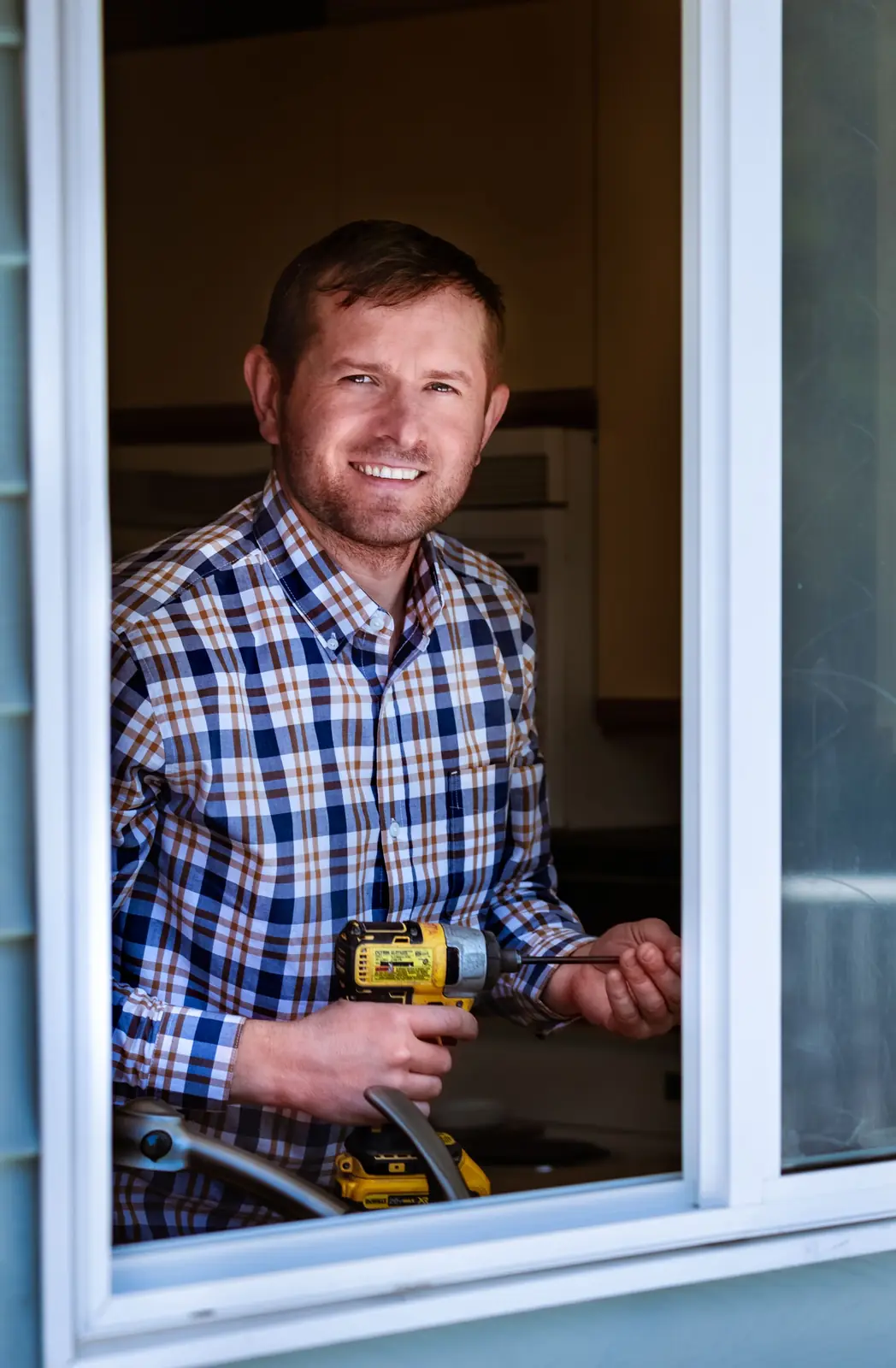 Digital marketing agency: smiling contractor holding a cordless drill at an open window of a home