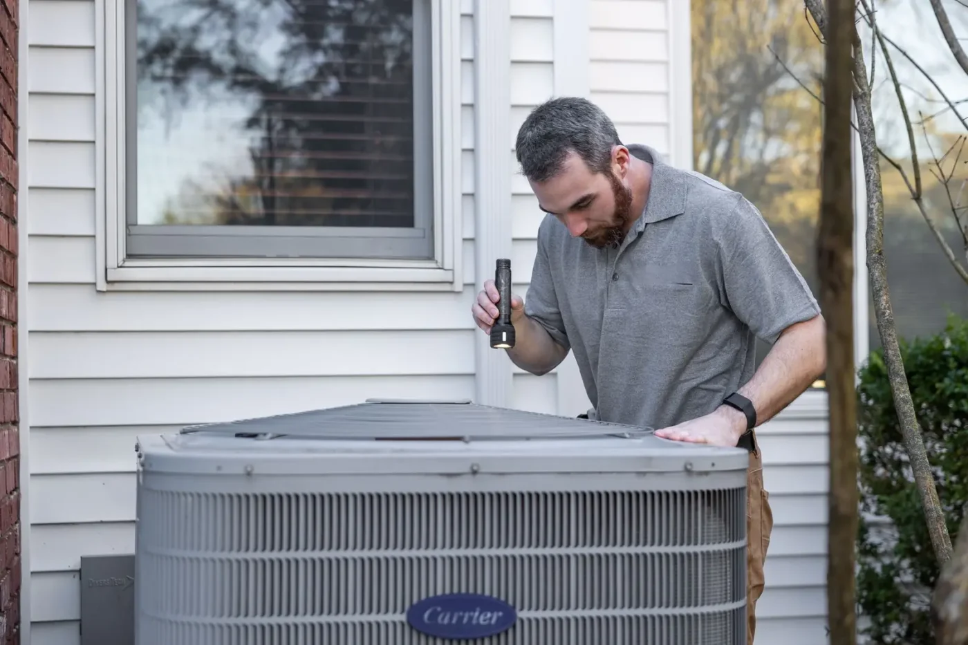 HVAC marketing: HVAC technician inspecting an outdoor air conditioning unit beside a home