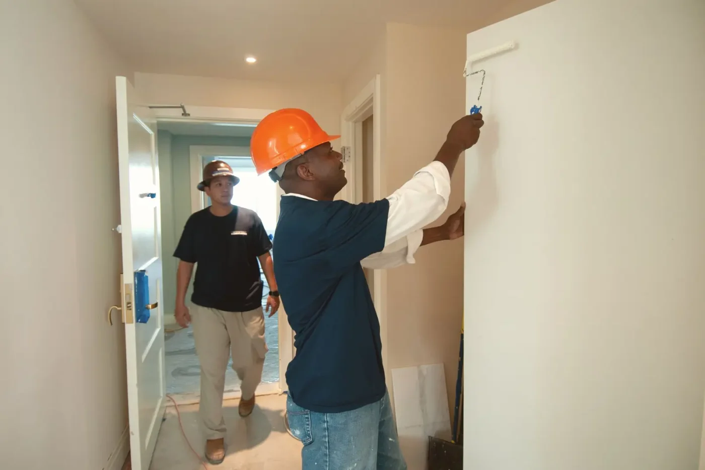 Painting company marketing: painter in a hard hat rolling paint onto an interior wall while a coworker walks in