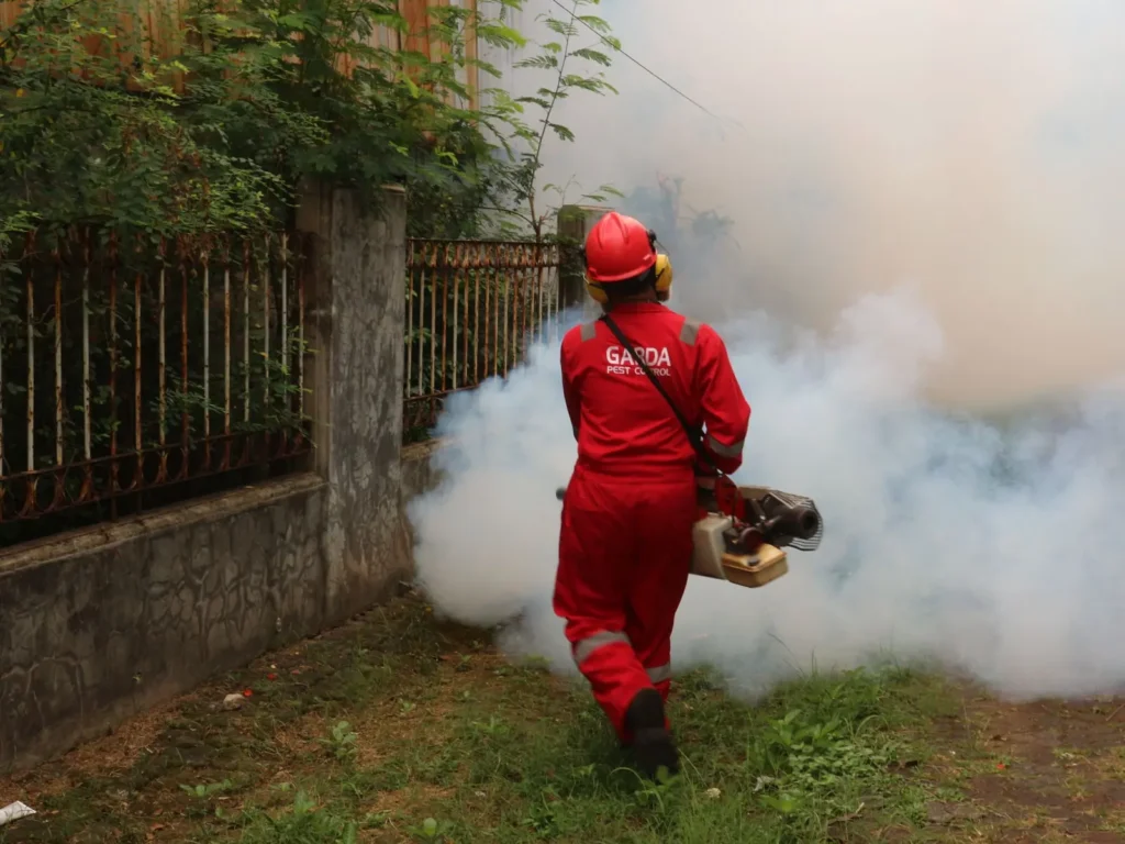 Pest control technician in a red suit fogging a backyard Pest control SEO: pest control technician in a red suit fogging a backyard