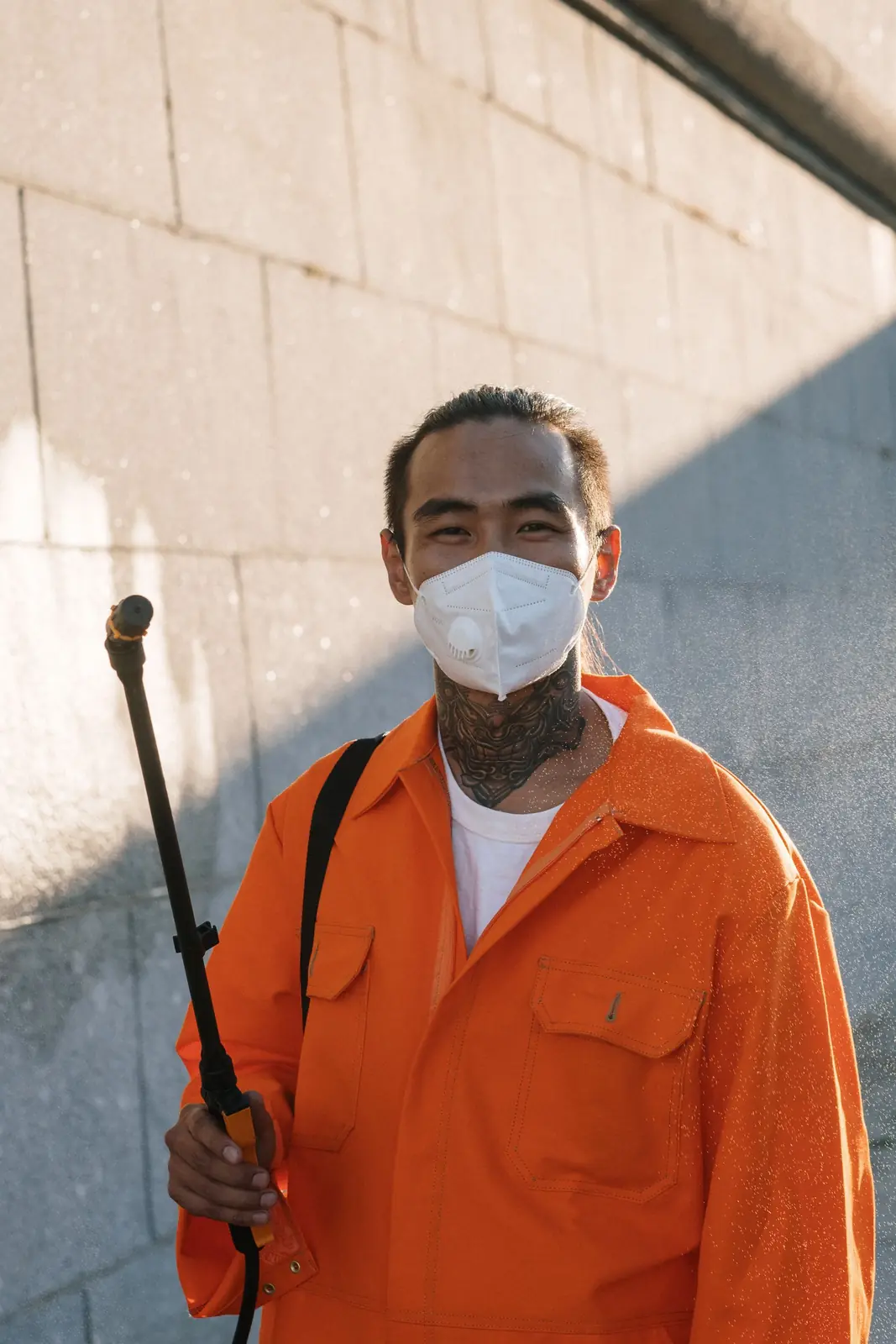 Pest control technician in orange coveralls and a face mask holding a sprayer wand Pest control SEO: pest control technician in orange coveralls and a face mask holding a sprayer wand